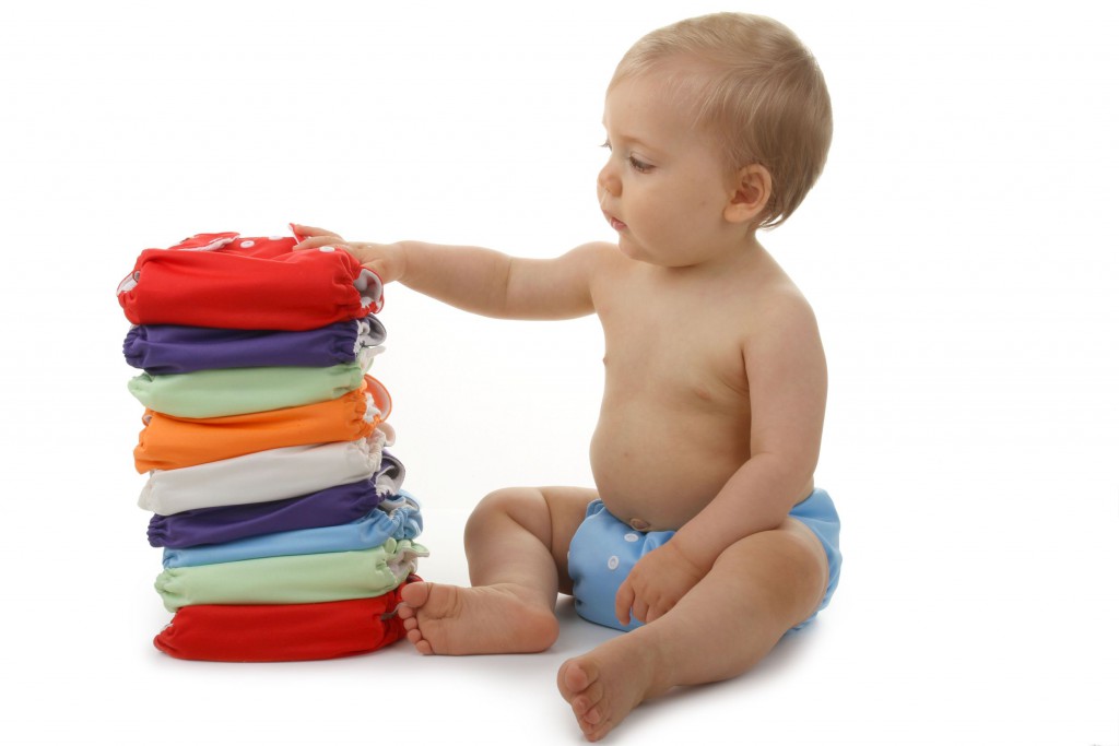 baby sitting with hand on a stack of colourful cloth diapers