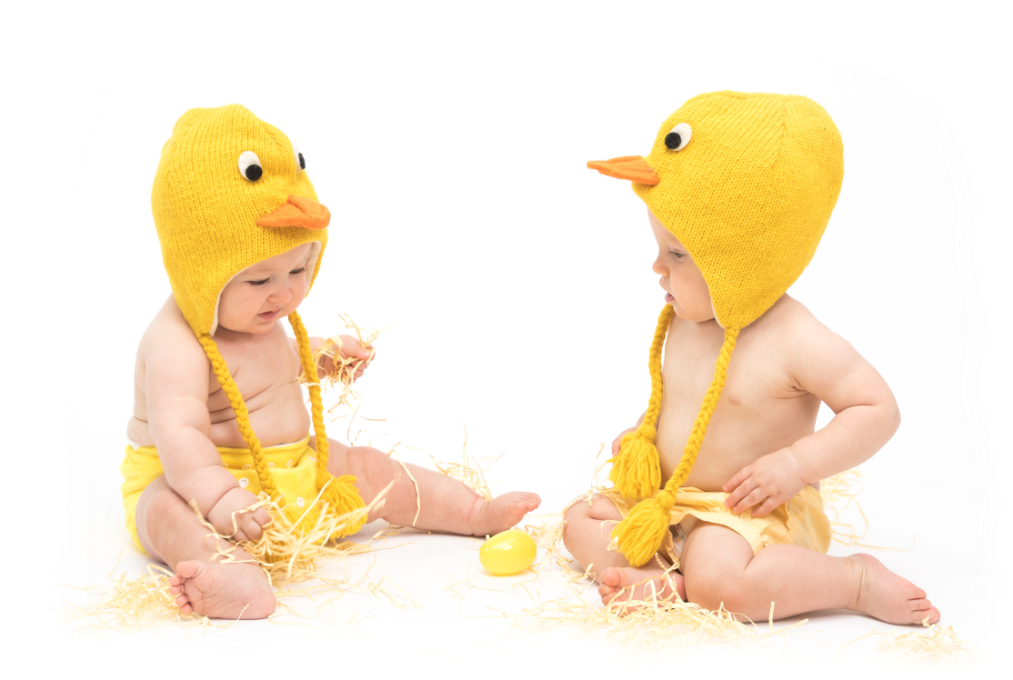two babies sat wearing duckling hats and yellow cloth diapers